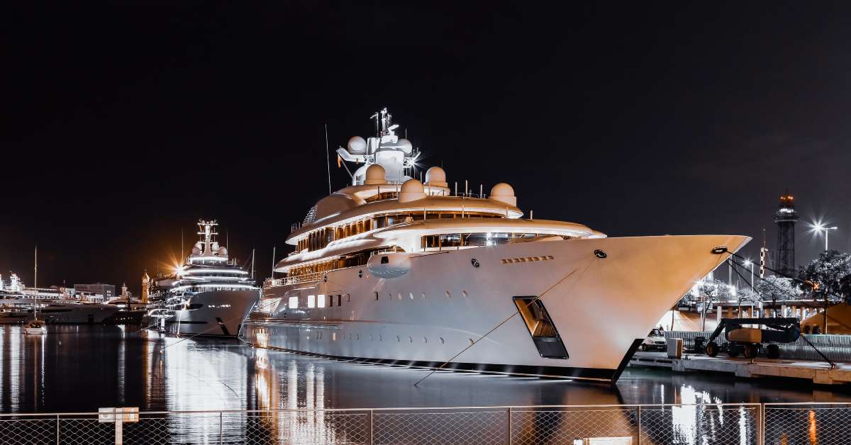 Two massive yacht charters sitting still against a small well-lit pier in the middle of the night.