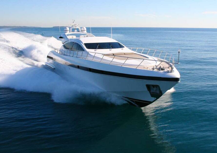 A large yacht is coasting through the dark blue water and causing large waves in its wake on a very sunny day.