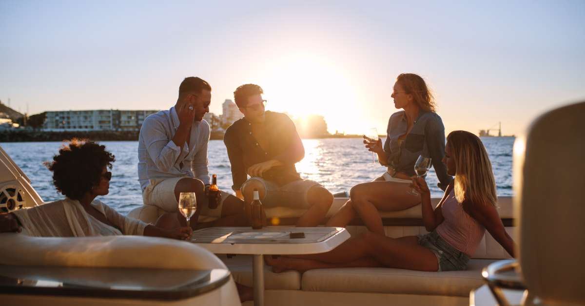 Five friends are sitting on the luxurious deck of a yacht, and the sun is setting behind them.