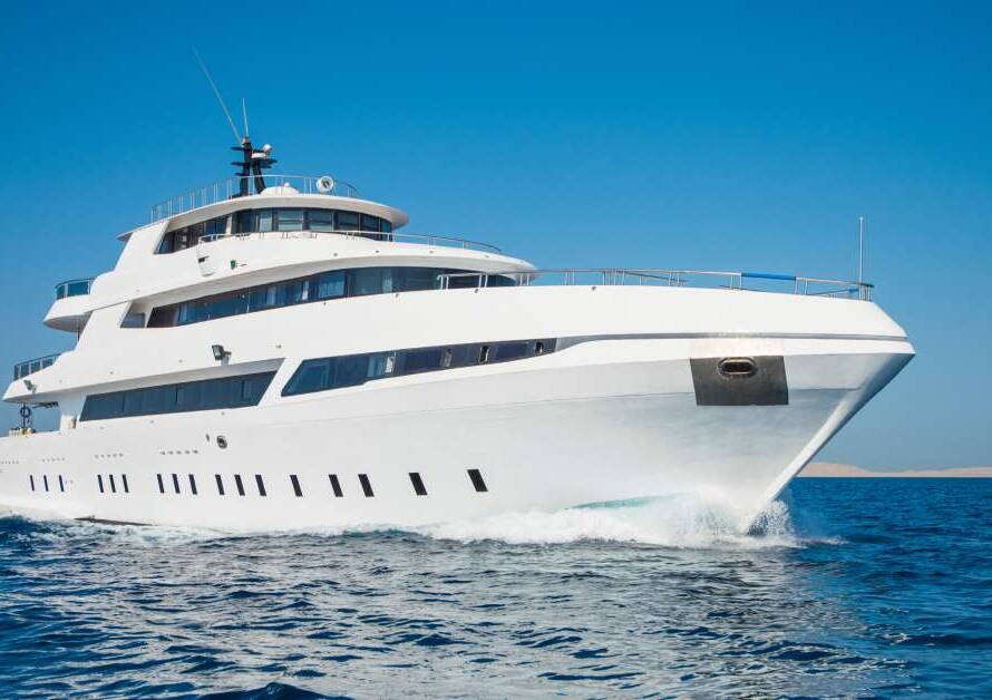 A white yacht that has several floors is coasting on the dark blue waters of the ocean. The sky above is clear and blue.