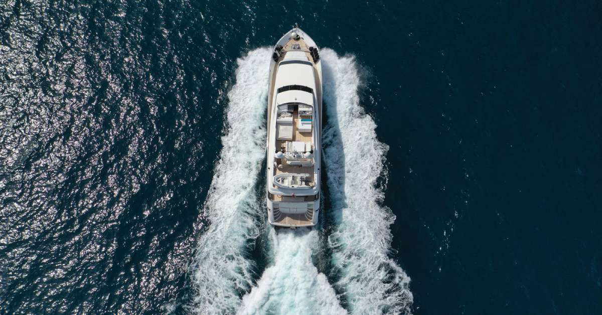 A large white yacht moving quickly on the ocean during a sunny day, causing massive waves in its wake.