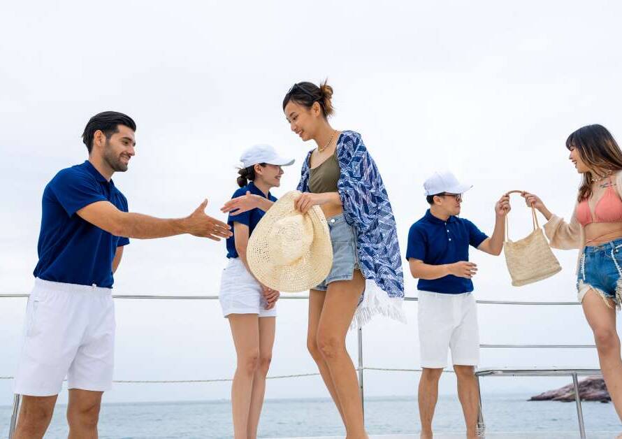 Two passengers stepping onto the deck of a private yacht while three crew members standby to offer assistance.