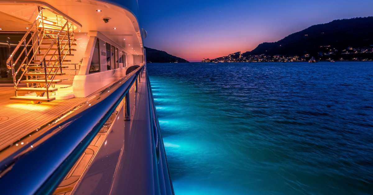 A multi-deck luxury yacht with bright lights on the decks and sides at night, illuminating the ocean around it.