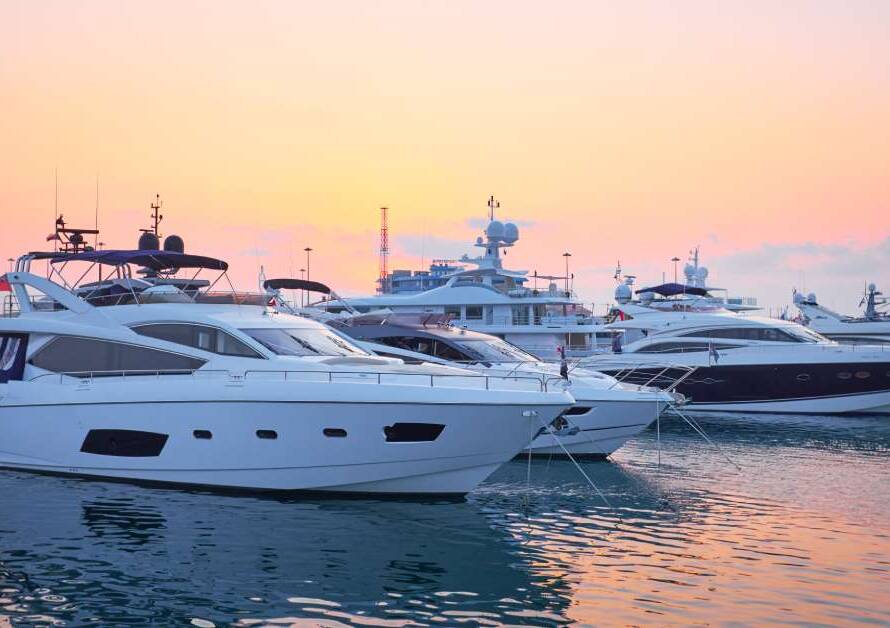 Seven yachts are parked at a pier. The orange sky is clearly reflected in the waters beneath the boats.