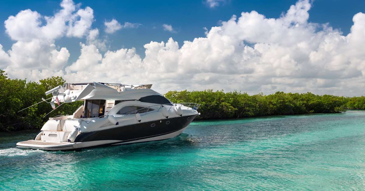 A large yacht coasts beside the green trees on a nearby island. The water is blue with a glass-like clarity.