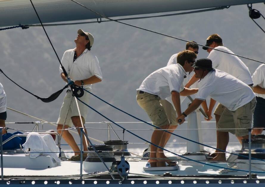 Seven crew members working on the deck of a white yacht. All crew members have dark sunglasses and a white shirt.